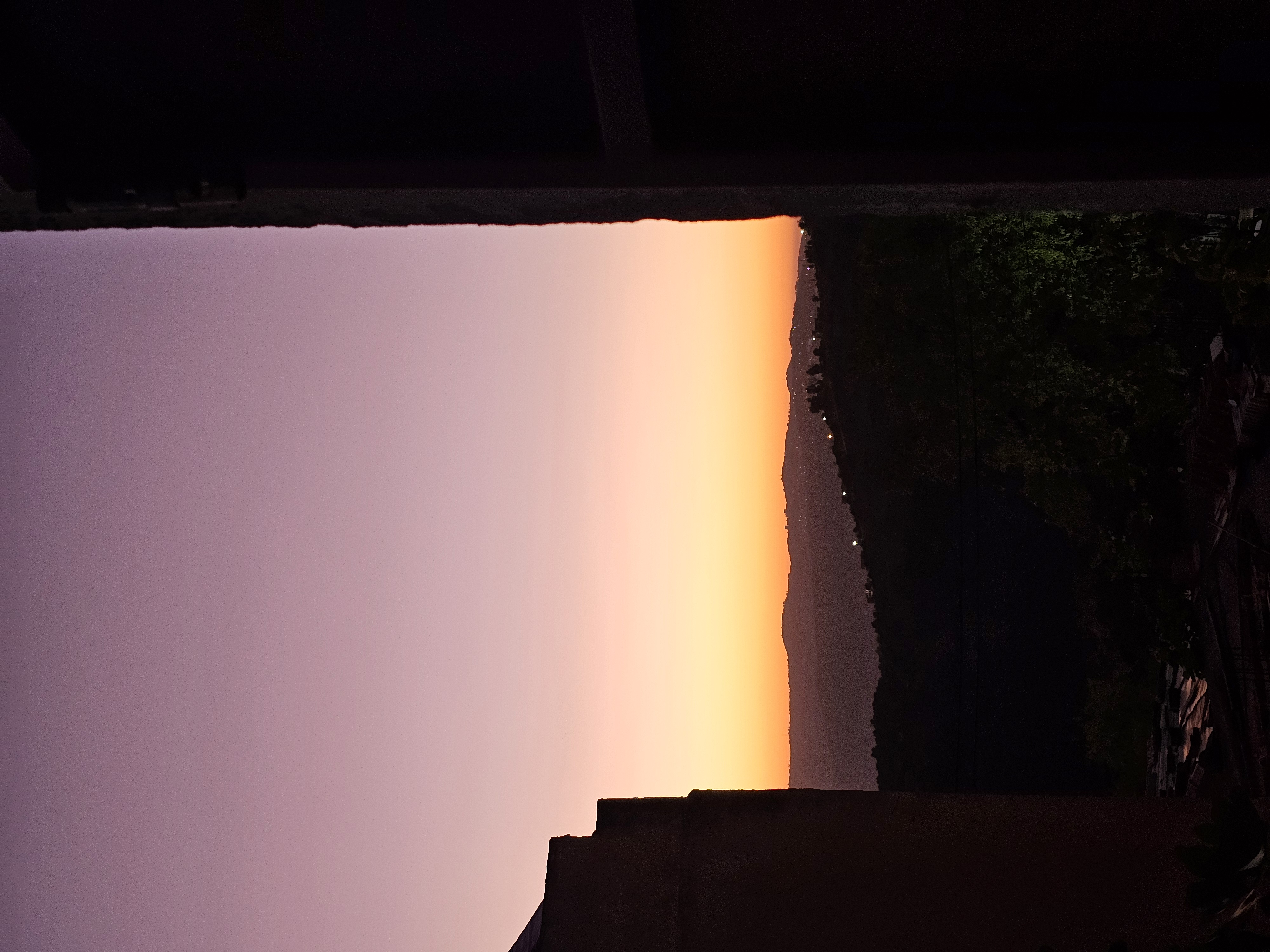 Un ciel rose et doré au-dessus des collines, encadré par deux bâtiments sombres.