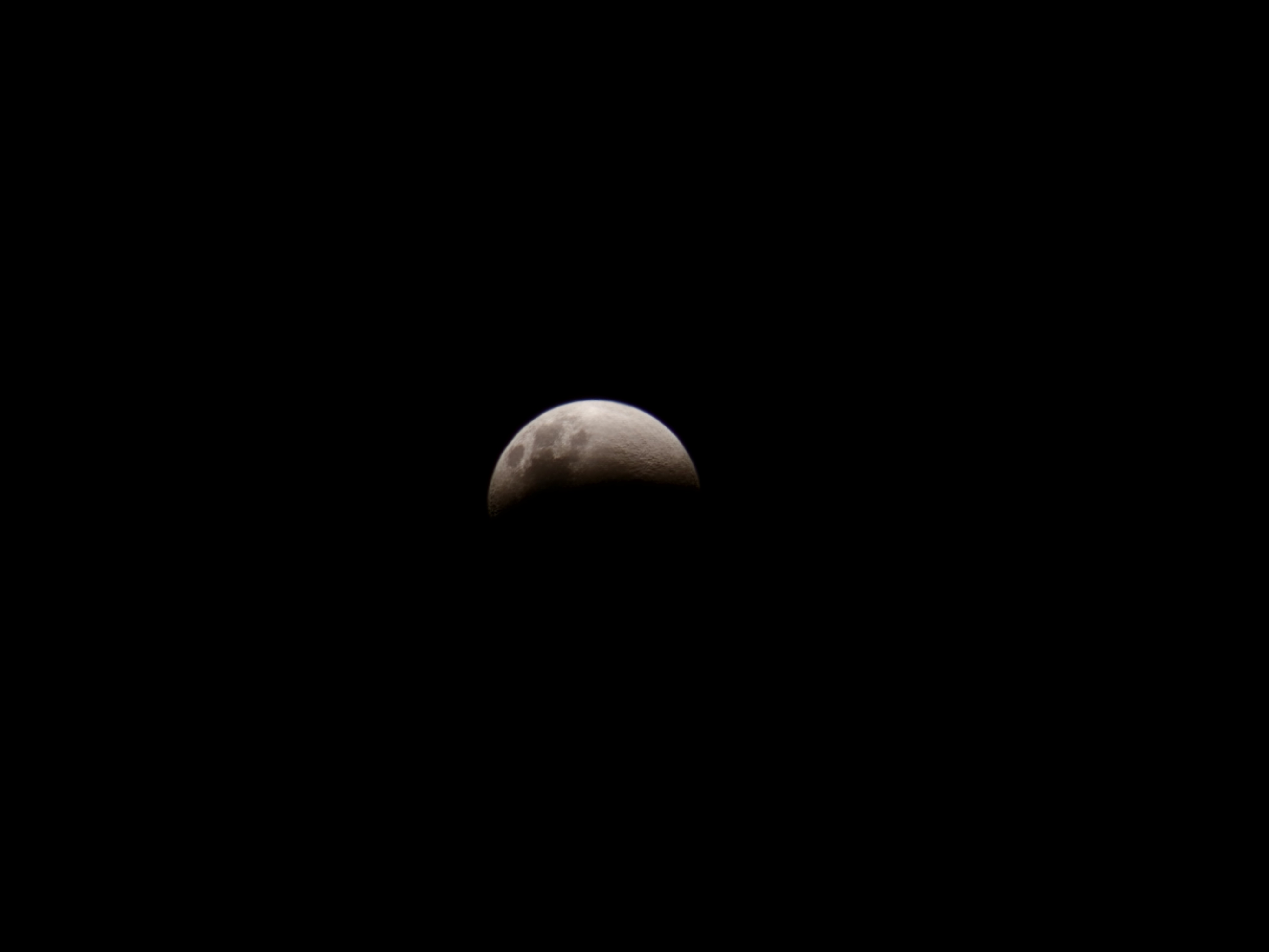 La lune partiellement éclairée dans un ciel noir.