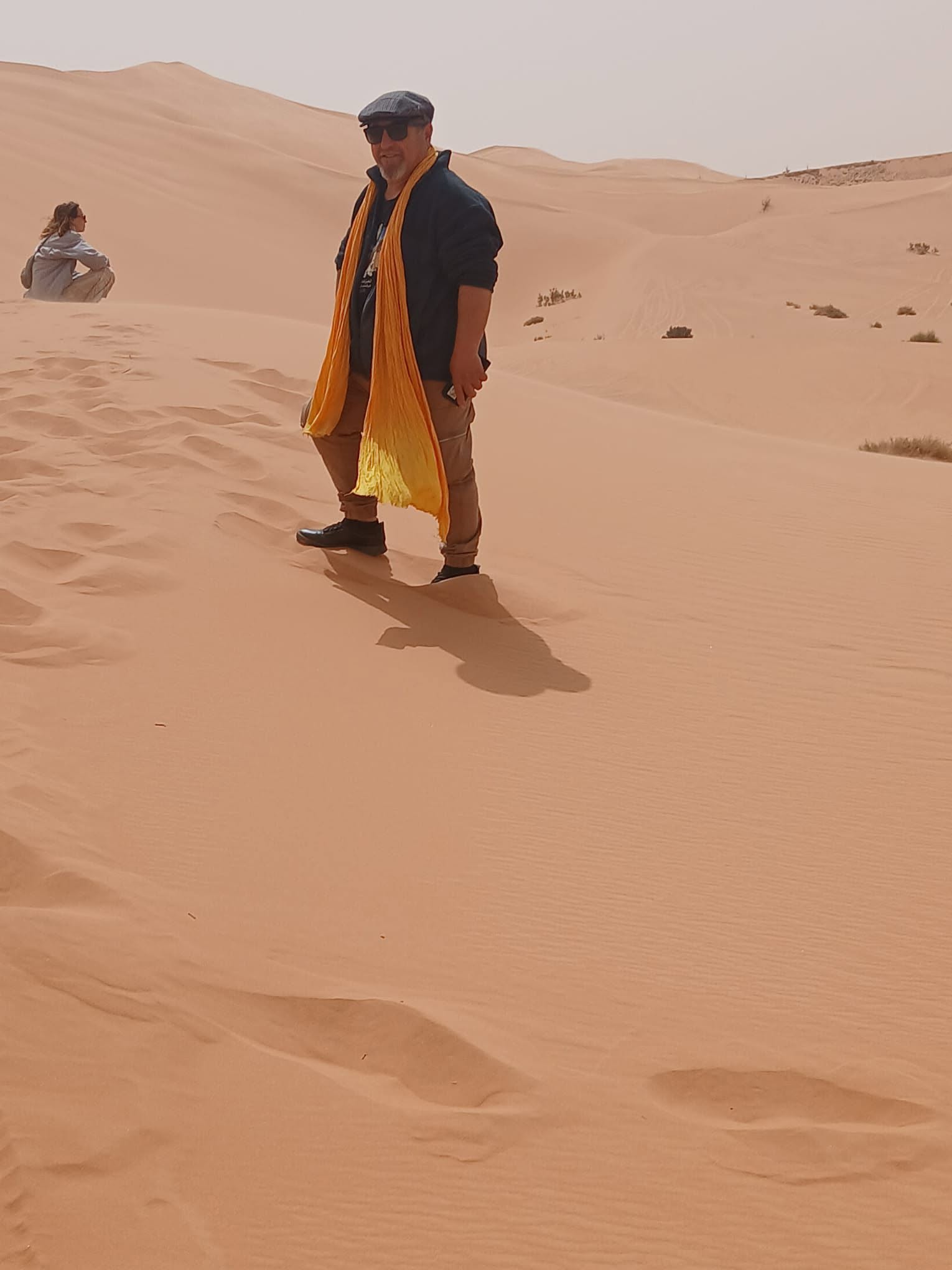 Un homme portant une écharpe jaune se tient parmi les dunes de sable.